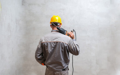 builder are holding a hammer drill and looking at the concrete wall view from his back