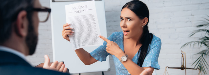 panoramic concept of displeased and brunette client pointing with finger at insurance policy agreement near lawyer in office