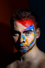 Portrait of a young man with colored paint on a dark background. Professional Makeup Fantasy Art Makeup