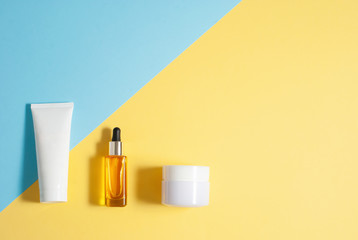 Cosmetic skin care yellow oil and white jars with creme on the colorful blue and yellow background flat lay top view
