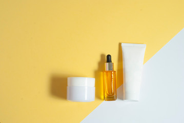Cosmetic skin care yellow oil and white jars with creme on the colorful white and yellow background flat lay top view