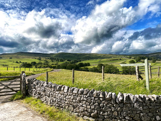 Farm track, with sign, next to a dry stone wall, with hills, valleys and farms in the distance, on a cloudy day in, Malham, Skipton, UK