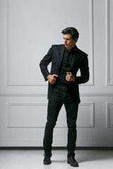 Full length photo of an stylish young man in black suit looking to his side, on white background.