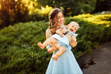 Overjoyed mother play with adorable daughter at the park, pretty woman hold baby girl in caring arms, smile, enjoy happy family moments, weekend outdoors, parenthood concept