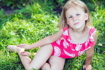 Little girl in pink swimsuit posing in summer grass
