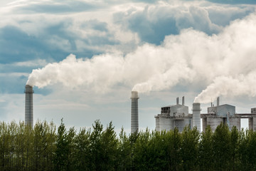 Industrial plant set in rural area spewing out big clouds of steam or smoke pollution against a blue sky