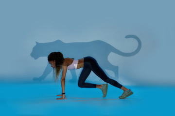 Fototapeta na wymiar As fast as cheetah. Full length shot of young sportive mixed race woman looking focused, standing in start position, ready for run isolated over pale blue creative art background with cheetah shadow