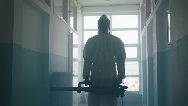 This video shows a man in protective overalls sanitizing a school corridor, spraying a disinfectant solution all over the passage.