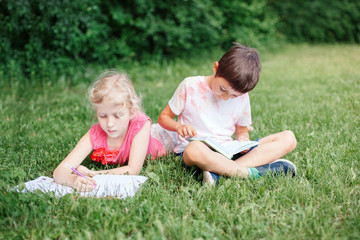 Naklejka na ściany i meble Elementary school students girl and boy doing homework outdoors. Children kids reading book and writing with pencil. Children education learning studying together. Friends classmates.