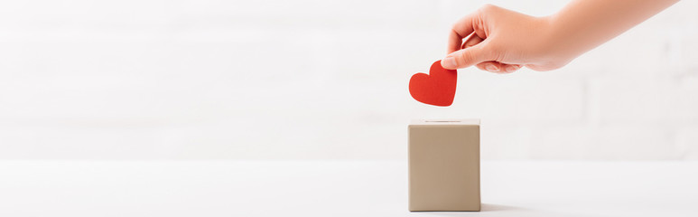 cropped view of female hand putting red heart in box on white background, donation concept