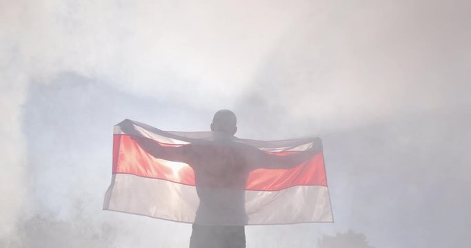 A man with the flag of Belarus in his hands stands in the smoke on the street at a peaceful protest.