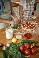 Pizza Day. Cropped shot of couple making pizza together at home. Man in apron adding basil on the dough while woman adding mozzarella cheese. Hobby, lifestyle