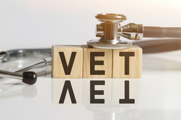 VET the word on wooden cubes, cubes stand on a reflective white surface, on cubes - a stethoscope.