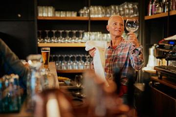 Waitress standing in bar and wiping wine glass.