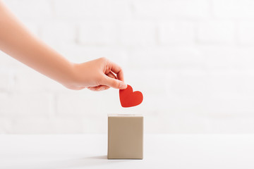 cropped view of female hand putting red heart in box on white background, donation concept - obrazy, fototapety, plakaty