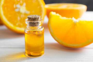 Natural orange essential oil in bottle and cut orange fruit on white wooden table.