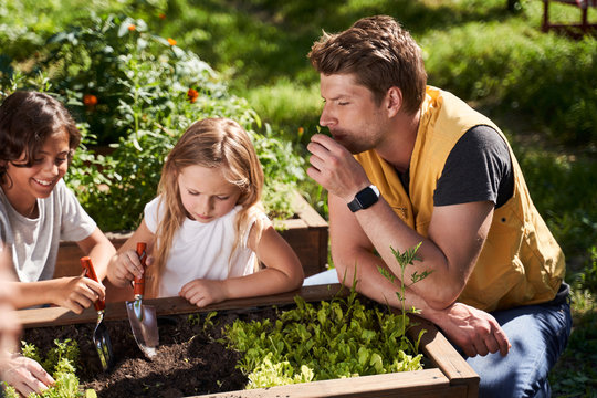 Adorable Kids Planting Flowers With Father In Garden