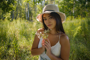 young brunette in a straw hat with wildflowers in her hands outdoors