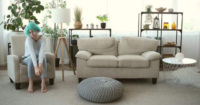 Bored or lazy woman with mint hair color sitting on armchair at home