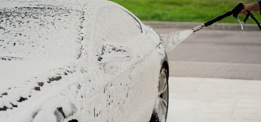 car wash with special windshield cleaning products. Professional detergents for car cleaning. Thick foam for protective application on the surface of the paint varnish. Care of the gray car.