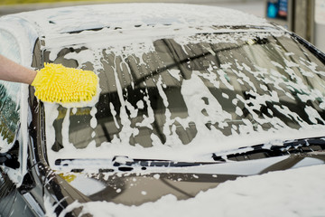 car wash with special cleaning products windshield. Professional detergents for car cleaning. Thick foam for protective application on the surface of the paint varnish. Care of the gray car.