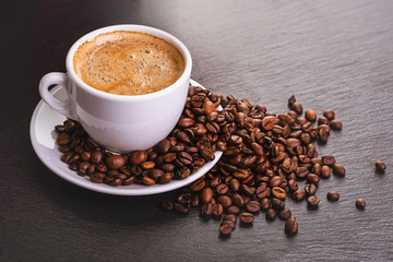 Coffee in a white cup with a saucer and coffee grains on a black background