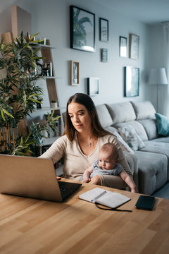 Young woman taking care of her baby while working at home