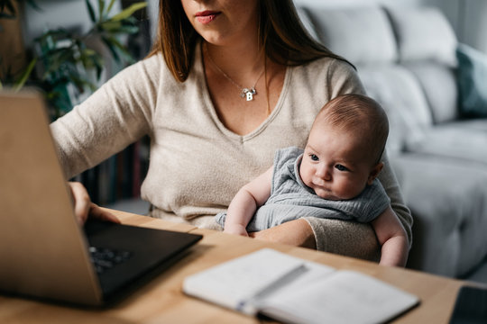 Anonymous young woman taking care of her baby while working at home