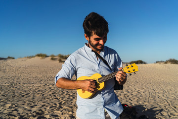 Hombre joven alegre cantando con un Ukelele en la playa