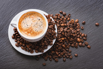 Coffee in a white cup with a saucer and coffee grains on a black background. View from above