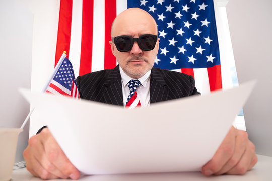 American intelligence officer. A man in black glasses on the background of the American flag. Secret agent in a tie in the colors of the us flag. USA intelligence officer.