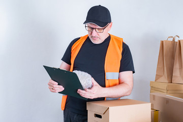 Online store. A man is engaged in packing goods for delivery. Remote sale of products. The courier accepts parcels for delivery. Online shop. Deliveryman.