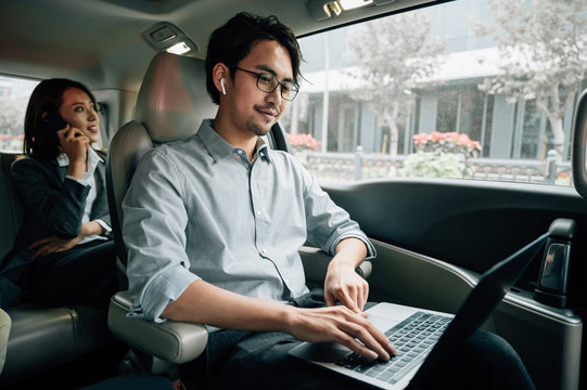 Businessman and businesswoman sitting in taxi and using laptop