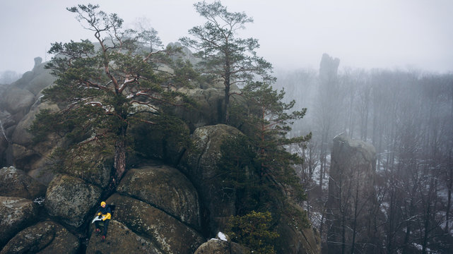 Traveler sitting on rocky hill among fog forest.