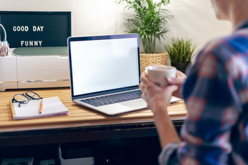 Cropped woman typing on laptop computer while sitting at home. Close up hands with mockup monitor and coffee cup. Distance learning online education and work.