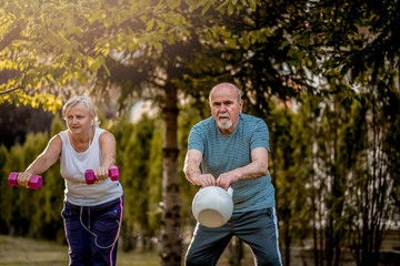 Healthy senior couple exercising with dumbbells and kettle bell