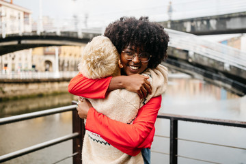 Happy multiracial best friends hugging on street