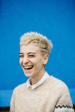 Cheerful young confident blond in casual clothes laughing against blue wall