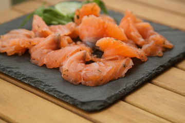 slices of lightly salted salmon on a black plate close up on a wooden table.