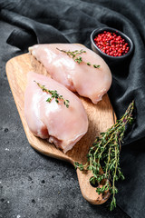 Raw chicken breast fillet on a chopping Board with herbs and spices. Black background. Top view