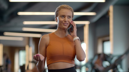 Confident athlete girl talking phone in sport club. Sportswoman standing at gym