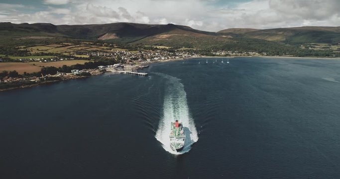 Scotland ocean, passenger ferry aerial view in coastal water of Firth-of-Clyde Gulf. Ship crossing from Brodick pier to Scottish mainland. Cityscape at green valleys. Footage shot in 4k, UHD