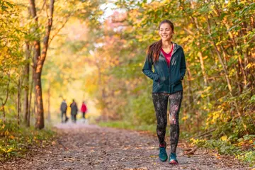 Foto op Plexiglas Woman walking in autumn forest nature path walk on trail woods background. Happy girl relaxing on active outdoor activity. © Maridav
