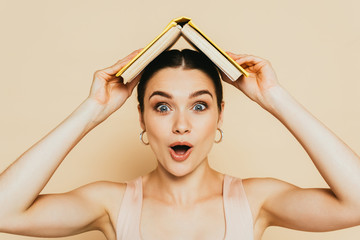 shocked brunette young woman with book on head on beige