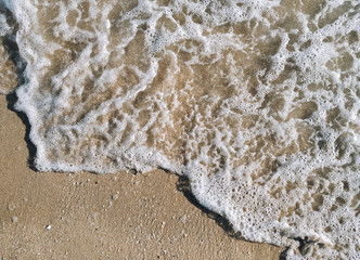 A sea wave with white foam rolls over the sand, top view. Copy space.