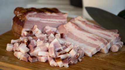 Smoked bacon meat with lots of fat on it, carved and diced on a wooded board.
The meat is salt-cured and from a pig's belly or back.