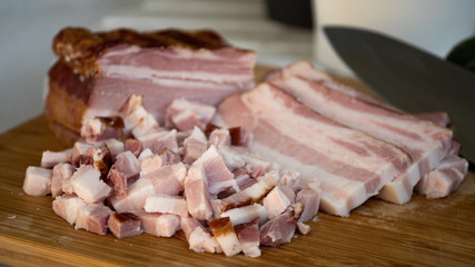Smoked bacon meat with lots of fat on it, carved and diced on a wooded board. The meat is salt-cured and from a pig's belly or back.