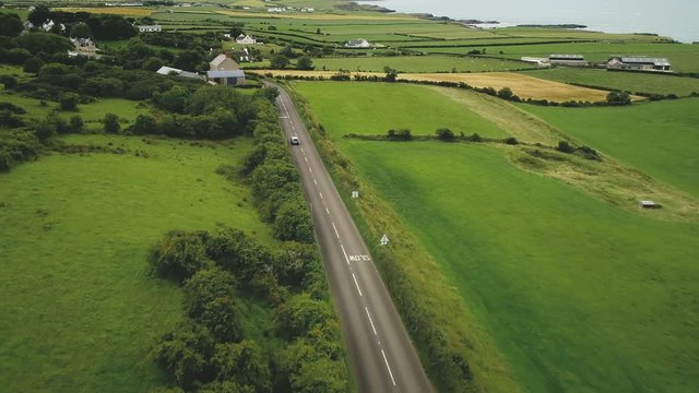 Ireland roadway car driving aerial view: green fields, meadows, farmland, cottages of Antrim County. Wonderful natural summer landscape overlooking ocean. Dramatic plot shot in FullHD