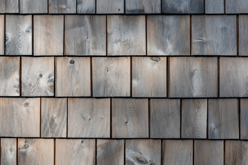 Natural white cedar shakes worn and textured on an exterior wall of a building. The thick smooth wood has faded in the sun. 