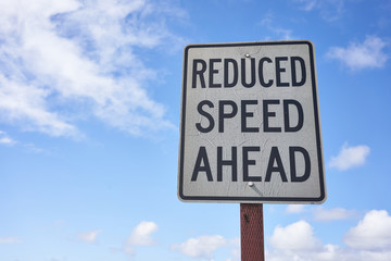 Reduced speed ahead sign against blue sky and clouds. Weathered road sign. Economic depression or...